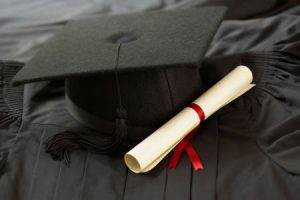 A graduation cap and gown with a diploma laying on top.