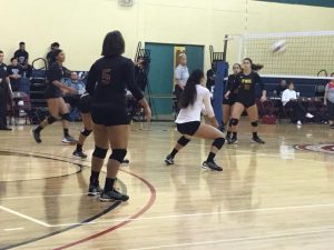 FNU volleyball player crouches down to hit ball. Other players watch.