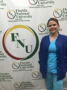 Woman wearing blue scrubs poses next to FNU logo