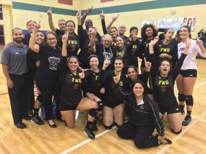 Volleyball players and FNU staff members hold up #1 with hand, celebrating their win