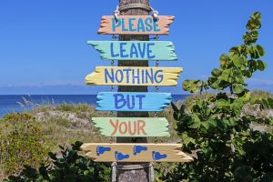 A sign made of driftwood on a beach that reads: please leave nothing but your footprints