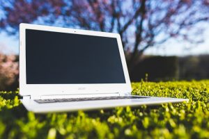 An open laptop computer atop green grass on a sunny day