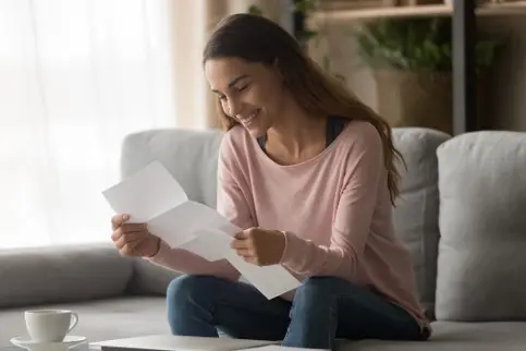 young women sitting on couch reading letter with a smile