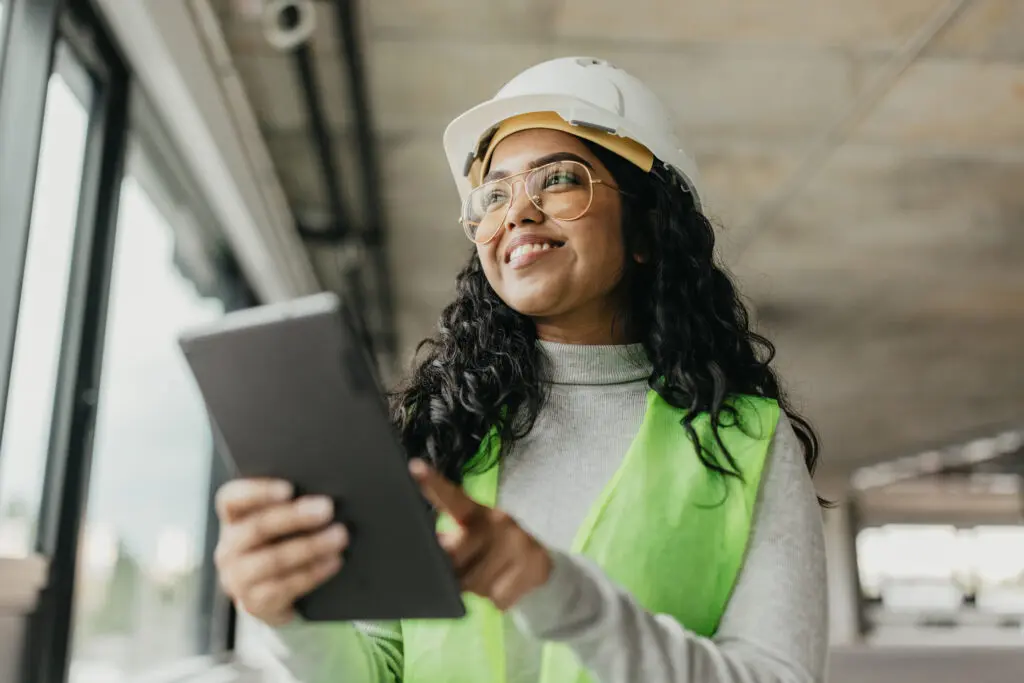 Engineer wearing a hard hat and safety vest, using a digital tablet on a construction site