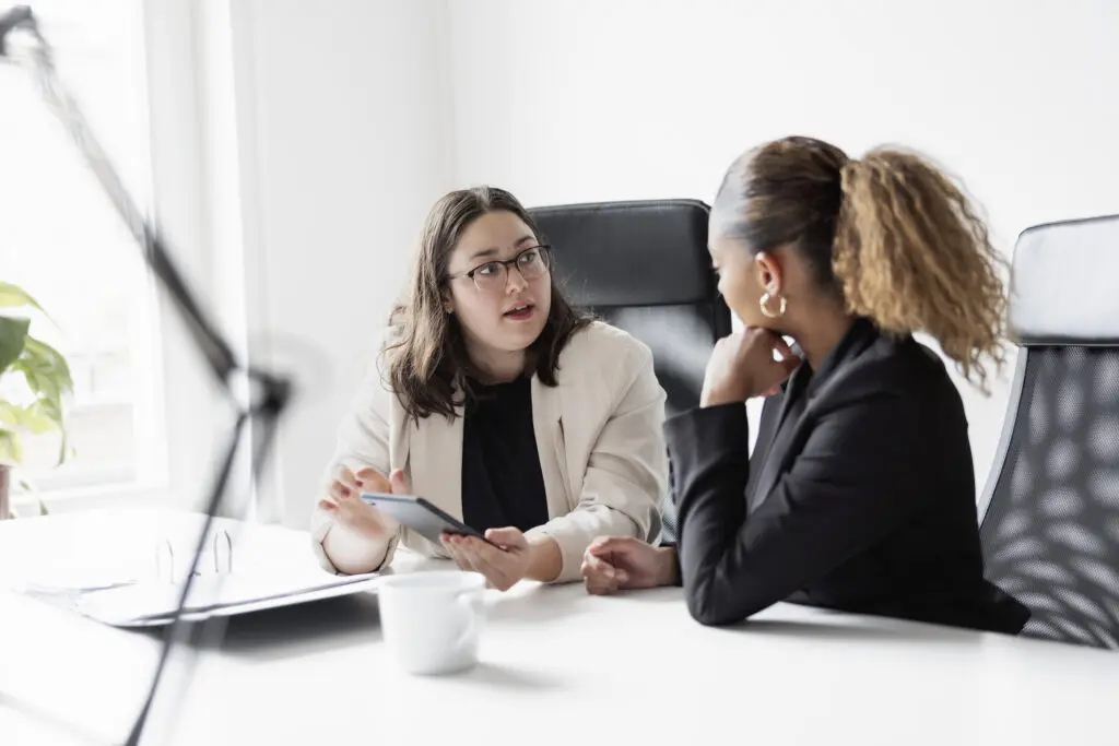 Two professional women discussing business strategy during a meeting, representing collaboration and career opportunities in business administration.
