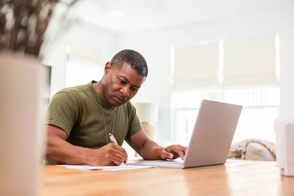 Veteran reviewing documents and using a laptop at home to explore GI Bill benefits for education and career training.