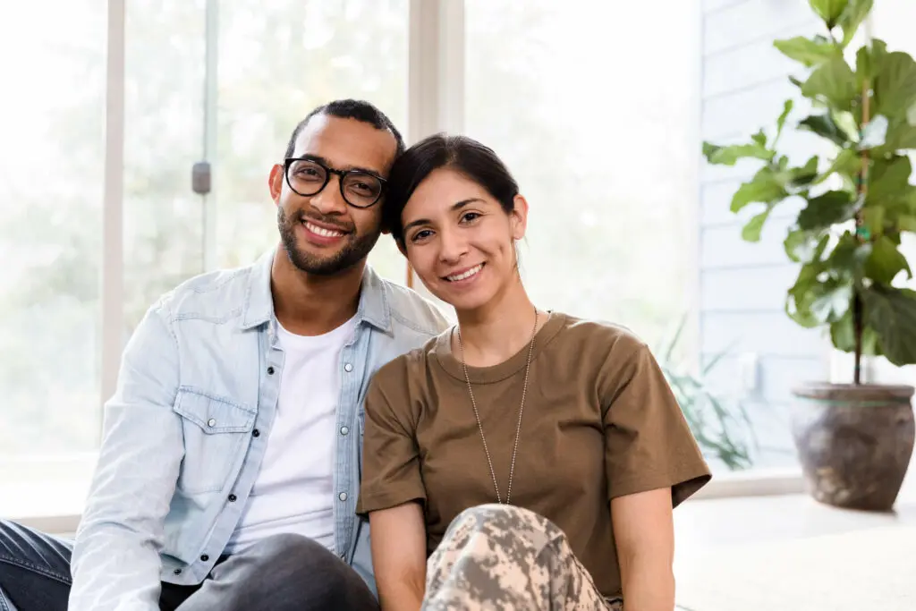 A military couple sitting on a couch, smiling.