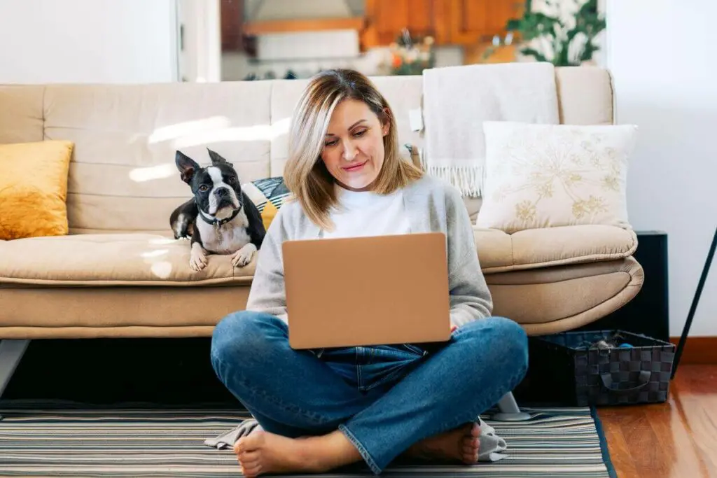 Woman sitting on the floor with a laptop and a dog, studying through an online degree program