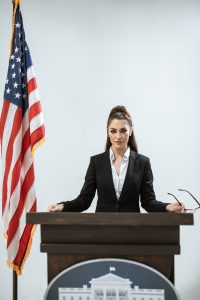 Lady standing at podium with American Flag. What is Public Administration?